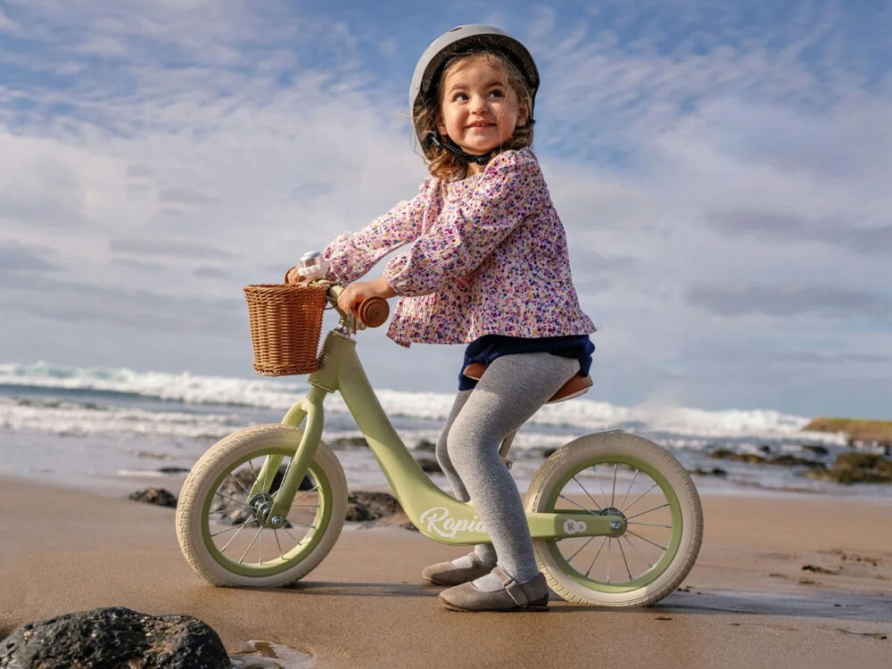Rowerek biegowy KINDERKRAFT Rapid 2 Różowy uśmiechnięta dziewczynka w kasku jedzie na zielonym rowerku gumowe uchwyty brązowy koszyk jasne koła plaża ze stopu magnezu Stop magnezu lżejszy od stali wytrzymały odporny na korozję waży zaledwie 3,7 kg manewrowanie przenoszenie bez trudu zdolność magnezu do skutecznego tłumienia drgań wyjątkowy komfort jazdy