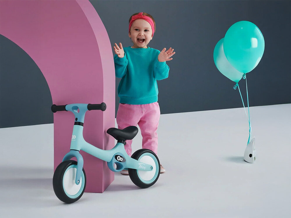 Rowerek biegowy KINDERKRAFT Tove Różowy rowerek w kolorze miętowym oparty o słupek gumowe uchwyty czarne siodełko obok stoi uśmiechnięte dziecko intuicyjny mechanizm montażu w zaledwie trzech prostych krokach kilka chwil przygoda na dwóch kołach wygoda dla zapracowanych rodziców praktyczny system składania bez zbędnych narzędzi i dodatkowych komplikacji