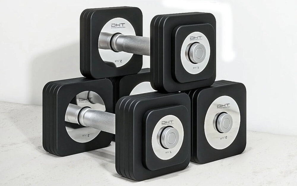 Na obrazie widoczne są cztery hantle z czarnymi, kwadratowymi obciążnikami i metalowymi uchwytami. Na obciążnikach znajduje się logo \'DHT\'.