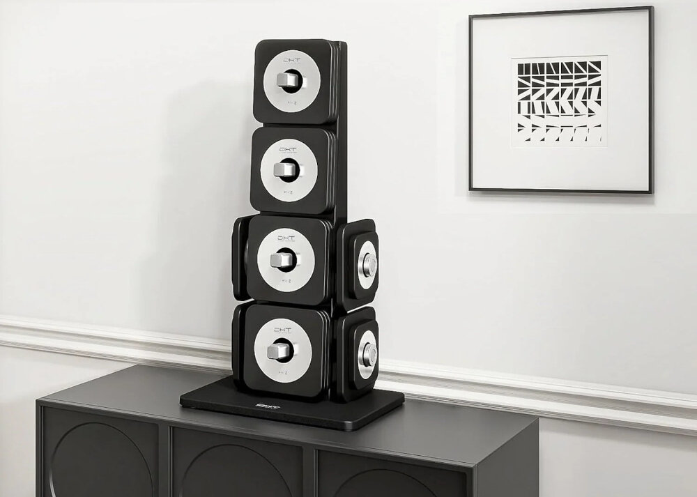 Na obrazie widać zestaw hantli ułożonych pionowo na czarnej podstawce z logo \'CHT\'. Obok na ścianie wisi obraz z geometrycznym wzorem w czarnej ramce.