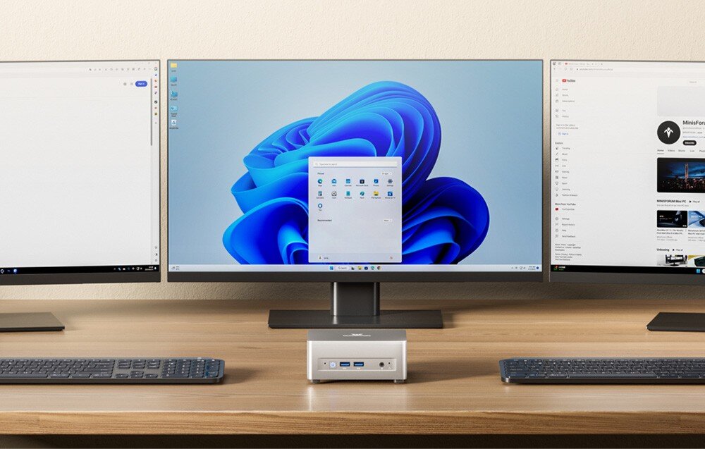 Komputer MINISFORUM UM870 Plus Srebrne urządzenie na biurku przed trzema monitorami wyświetlającymi pulpit Windows i stronę YouTube.