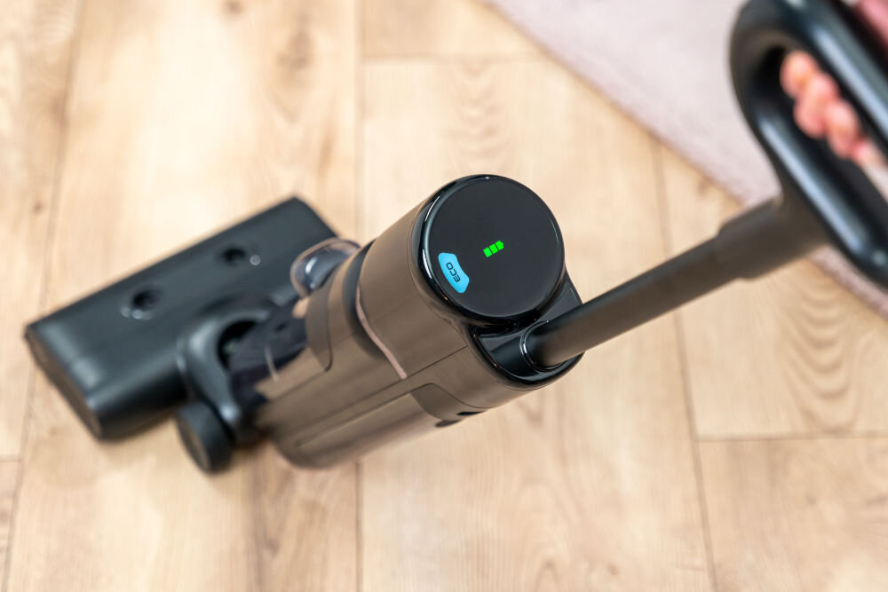 Odkurzacz mopujący GÖTZE & JENSEN VM500 Widok z góry na odkurzacz pionowy GÖTZE & JENSEN VM500 pracujący na panelach podłogowych w trybie ECO z widocznym wskaźnikiem naładowania baterii.