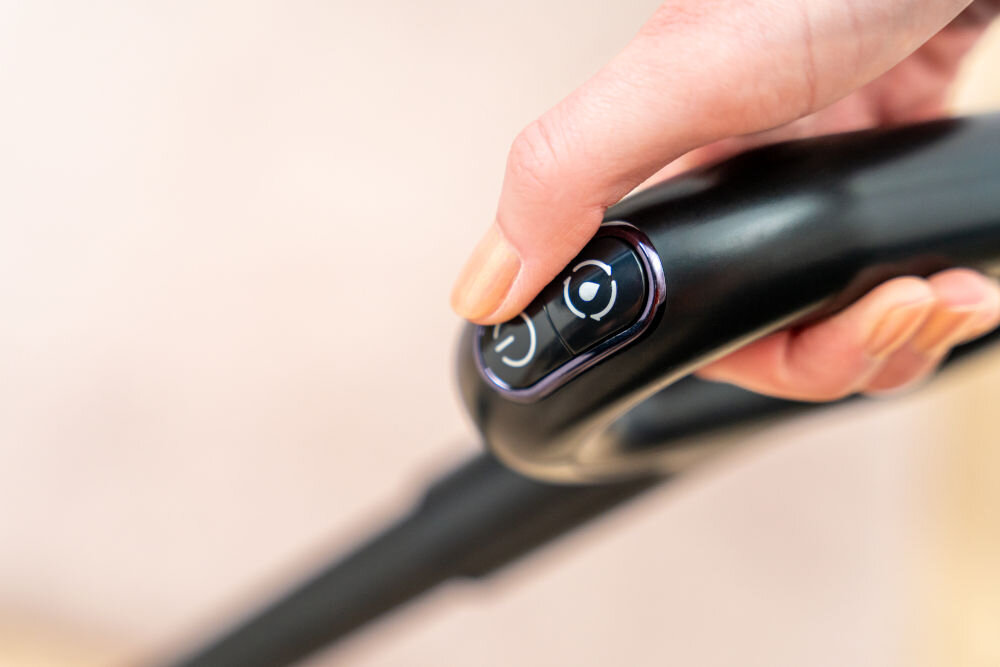 Odkurzacz mopujący GÖTZE & JENSEN VM500 Ręka użytkownika naciskająca przyciski sterowania na ergonomicznym uchwycie odkurzacza bezprzewodowego GÖTZE & JENSEN VM500.