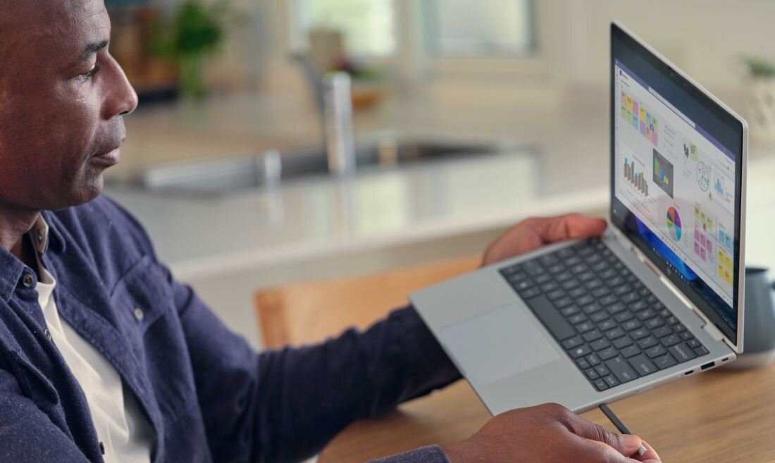Mężczyzna w niebieskiej koszuli pracujący na laptopie HP EliteBook X Flip w jasnej kuchni, na ekranie kolorowe wykresy i dane analityczne, koncentracja na pracy z danymi biznesowymi. - Klawiatura odporna na ciecz i na zalanie