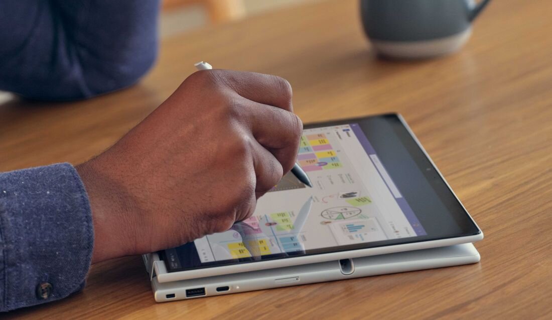 Zbliżenie na dłoń trzymającą piórko cyfrowe nad laptopem HP EliteBook X Flip w trybie tabletu, na ekranie kolorowe wykresy i diagramy biznesowe z żółtymi notatkami, na drewnianym biurku. - Dysk SSD PCIe NVMe