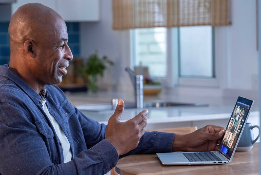 Mężczyzna w niebieskiej koszuli gestykulujący podczas wideokonferencji na laptopie HP EliteBook X Flip w jasnej kuchni, na ekranie widoczne okna rozmowy wideo z innymi uczestnikami spotkania. - Kamera IR 5MP z AI 