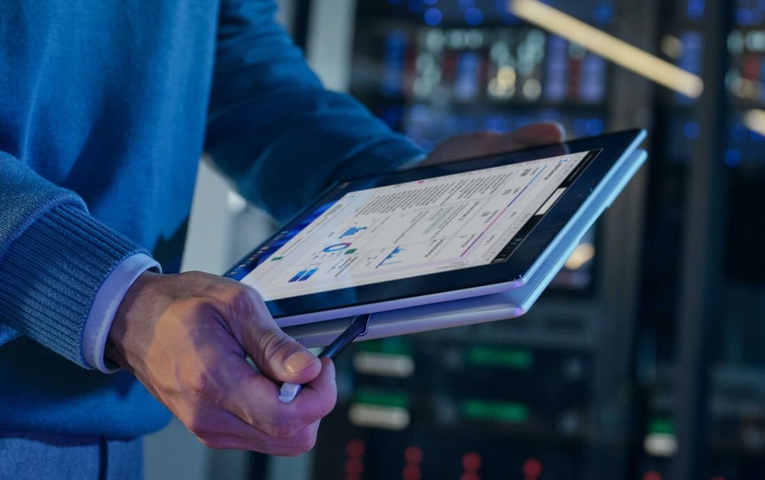 Mężczyzna w niebieskim swetrze trzymający laptop HP EliteBook X Flip w trybie tabletu w przemysłowym środowisku z serwerami w tle, podkreślający funkcje bezpieczeństwa HP Sure Click w środowisku korporacyjnym. - HP Sure Click