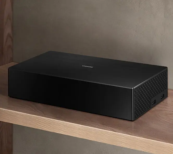 Na brązowej półce leży prostokątny, czarny moduł One Connect