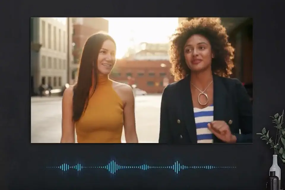 Telewizor z dwoma kobietami na ekranie, poniżej grafika fali dźwiękowej symulująca dostosowanie się dźwięku do sceny.