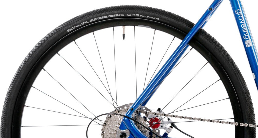 Rower gravel ROMET Boreas 1 U21 28 cali Biało-niebieski zbliżenie na tylną oponę rozmiar koła 28 cali opony SCHWALBE bardzo dobra przyczepność trwałość komfort jazdy aluminiowe obręcze Alexrims ATD550 stabilne trzymanie opony sprzęt do wyczynowego kolarstwa szybkiego regularne sprawdzanie ciśnienia powietrza wartość na bocznej części opony