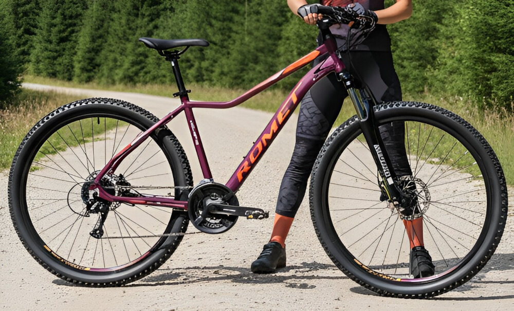 Rower górski MTB ROMET Jolene 7.2 JA D19 27.5 cala damski Purpurowo-pomarańczowy góry droga niebo osoba jedzie na rowerze po drodze kierownica RMT Components 680 x 31,8 mm aluminiowy wspornik ROMET 90/31,8 mm stabilność precyzja prowadzenia antypoślizgowe uchwyty kontrola nad rowerem i bezpieczeństwo waga roweru 14 kg