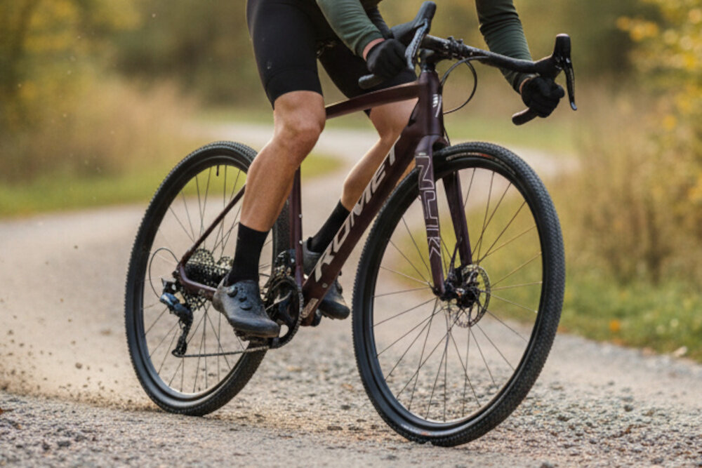 Rower gravel ROMET Nyk U23 28 cali Brązowo-beżowy 2024 droga las łąka osoba jedzie na rowerze po drodze karbonowa kierownica marki ROMET redukuje drgania przenoszone z nawierzchni szerokość 420 mm oferuje stabilną pozycję i precyzyjne prowadzenie aluminiowy mostek ROMET wysoka sztywność połączenia trwałość pewne i przewidywalne sterowanie 