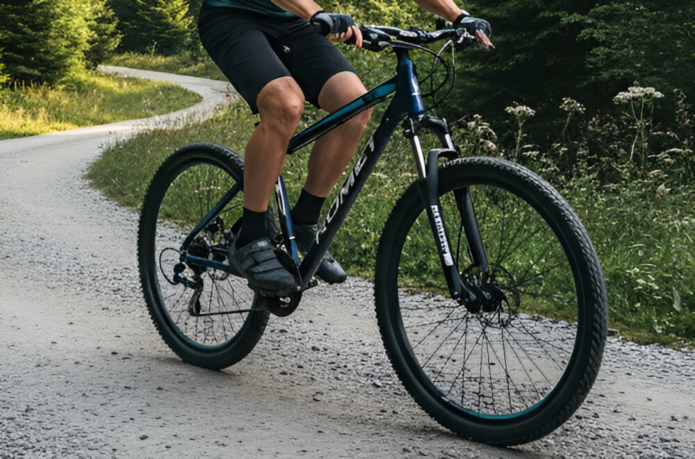 Rower górski MTB ROMET Rambler R7.1 U21 27.5 cala Granatowy góry droga niebo osoba jedzie na rowerze po drodze kierownica RMT Components 720 x 31,8 mm aluminiowy wspornik ROMET 90/31,8 mm stabilność precyzja prowadzenia antypoślizgowe uchwyty kontrola nad rowerem i bezpieczeństwo waga roweru 15,2 kg