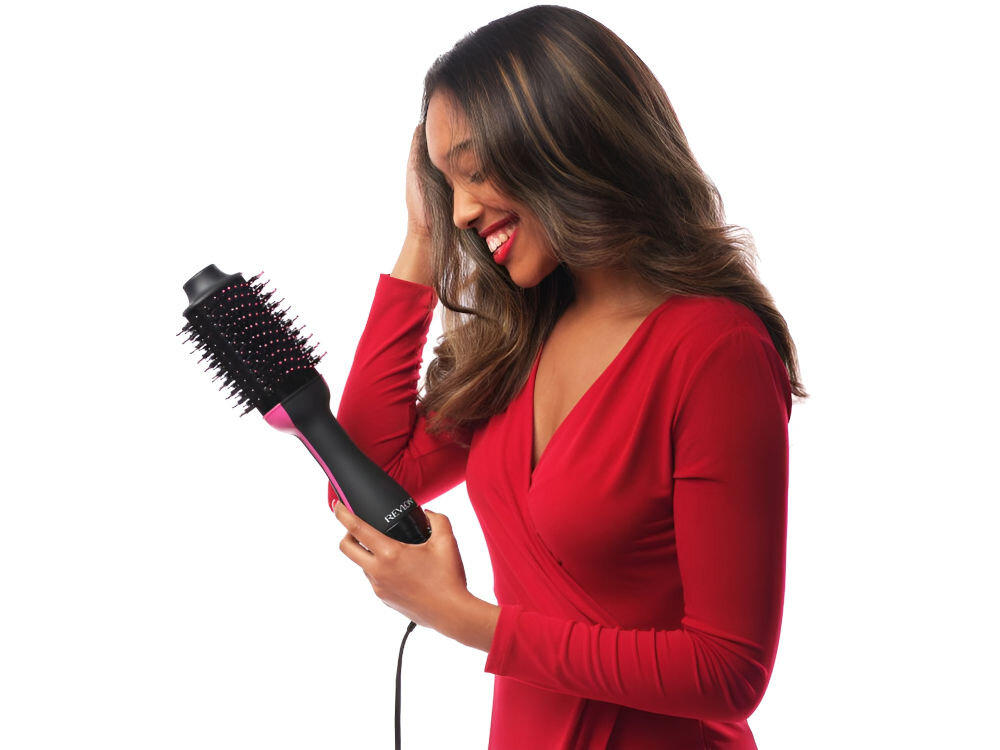 Osoba trzyma czarną suszarko-lokówkę z widocznym napisem \'REVLON\'. Urządzenie ma okrągłą szczotkę z kolcami.