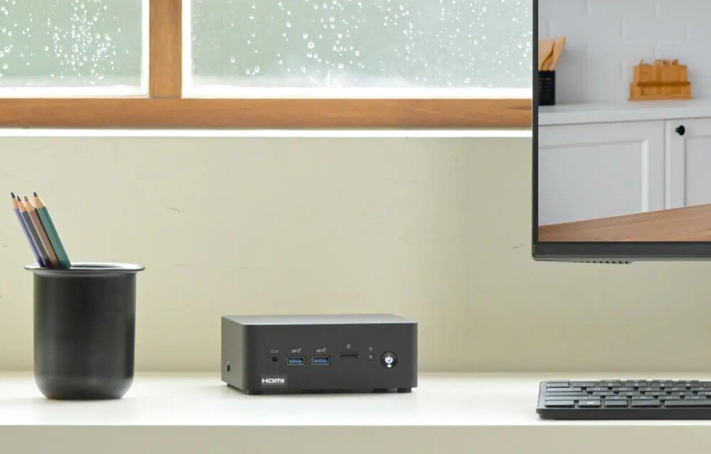 Komputer MSI Cubi NUC AI+ 2MG-007EU Niewielki komputer ustawiony na biurku obok kubka z ołówkami i monitora, w tle jasne wnętrze z oknem, chłodzenie