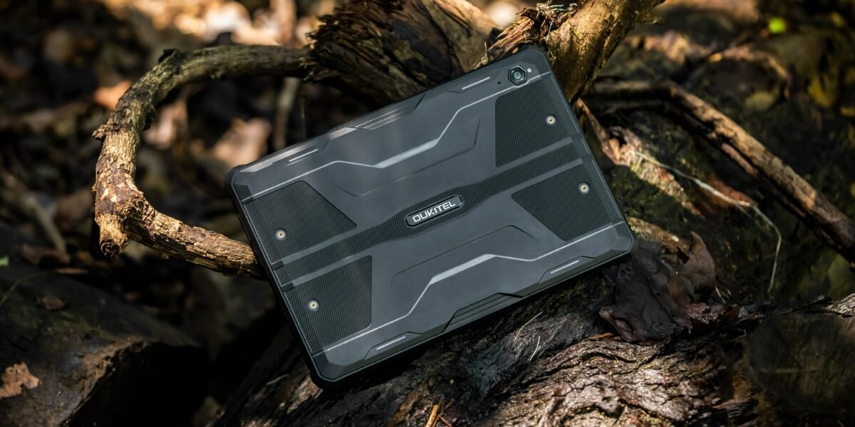 Tablet w kolorze czarnym leży na drewnianym pniu w lesie. Na obudowie widoczne jest logo \'OUKITEL\'.