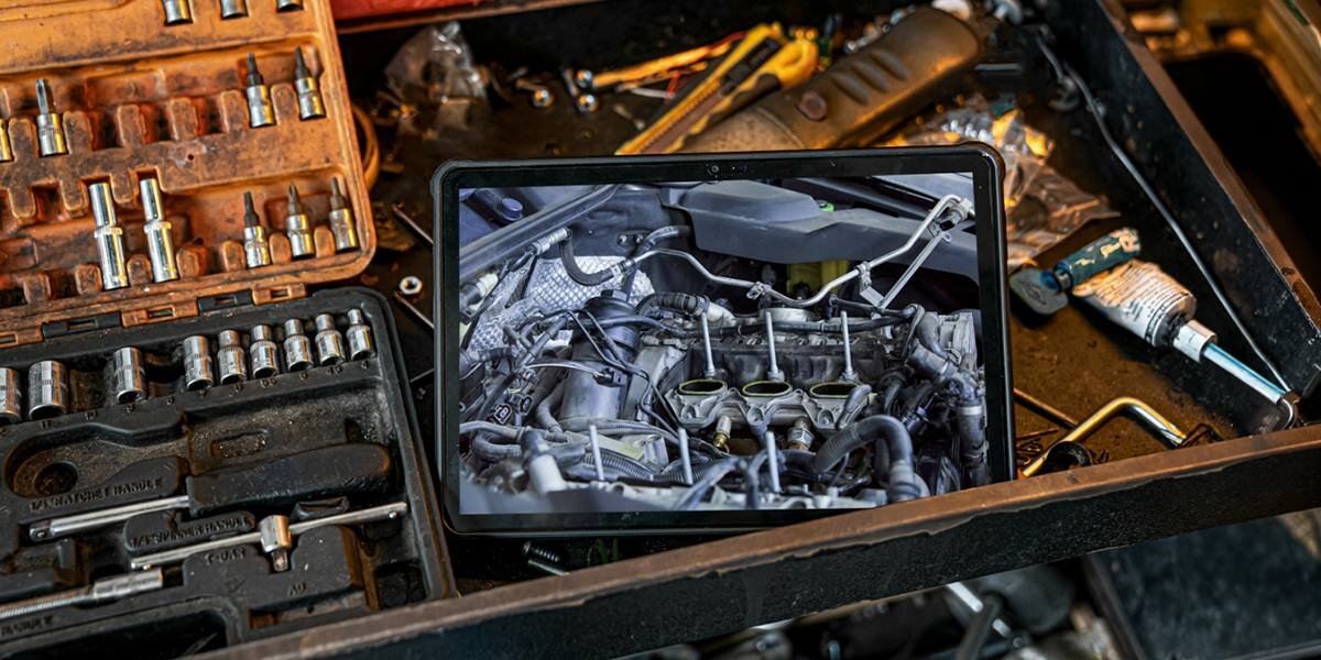 Tablet wyświetla obraz silnika samochodowego, leżąc na blacie roboczym wśród narzędzi mechanicznych, takich jak klucze nasadowe i śrubokręty.