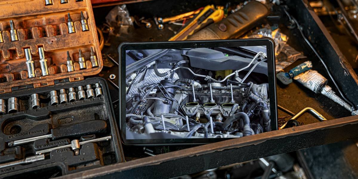 Tablet wyświetla obraz silnika samochodowego, leżąc wśród narzędzi warsztatowych, takich jak klucze i nasadki.