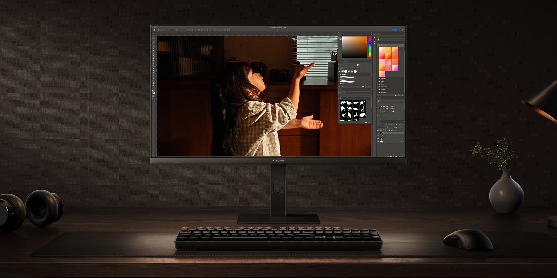 Monitor XIAOMI na biurku na ciemnym tle, na monitor pada światło z lewej strony.