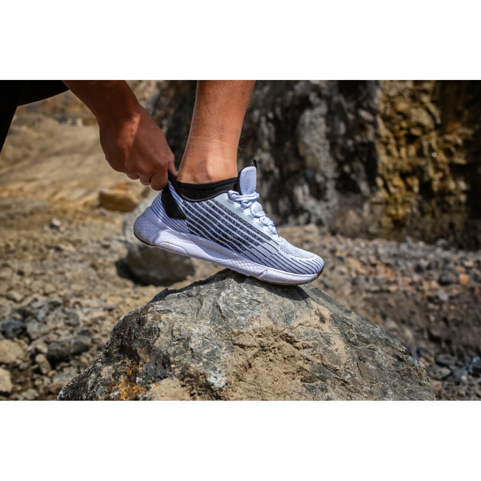 Osoba zakłada jasne, sportowe buty na skale w naturalnym, skalistym otoczeniu.