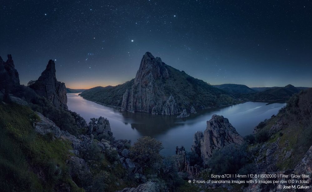 Nocny krajobraz przedstawiający rzekę otoczoną górami pod rozgwieżdżonym niebem. W prawym dolnym rogu widoczny jest tekst: \'Sony α7CII | 14mm | f/2.8 | ISO2000 | Filter: Glow filter * 2 rows of panorama images with 5 images per row (10 in total) © Jose M. Galvan\'.