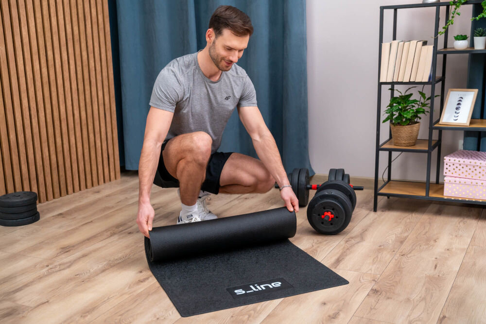 Mata pod sprzęt fitness S-LINE M4 SA034 Mężczyzna zwijający czarną matę fitness S_line po treningu siłowym w domu.