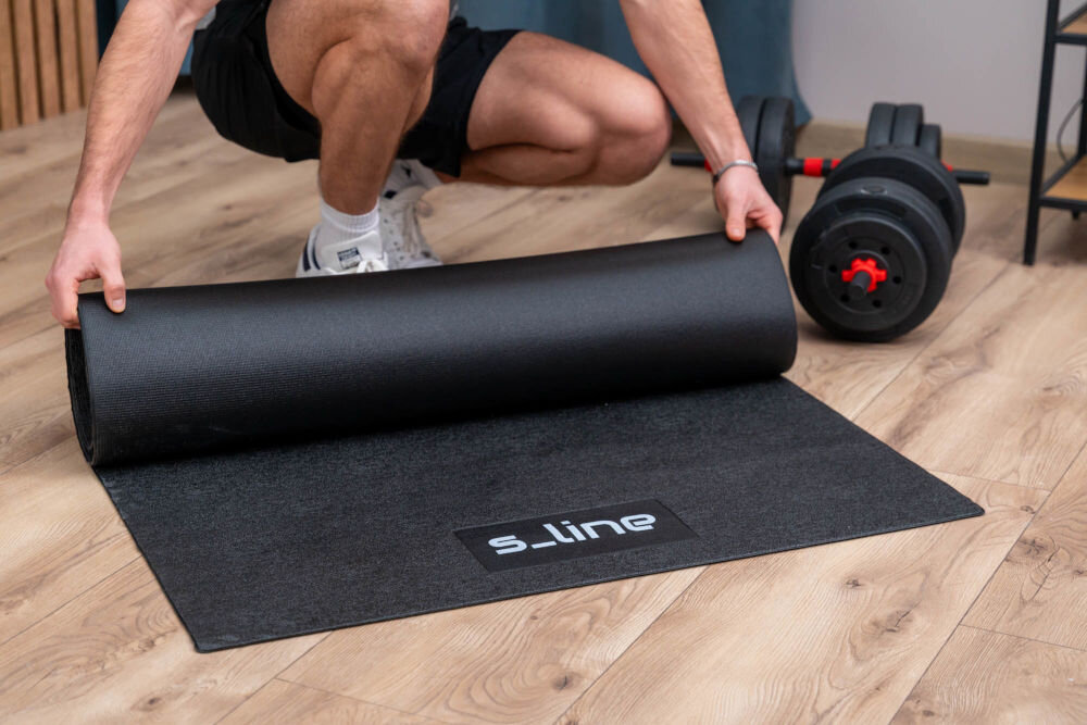 Mata pod sprzęt fitness S-LINE M4 SA034 Zbliżenie na dłonie mężczyzny zwijającego grubą matę fitness S_line z widocznym logo marki.