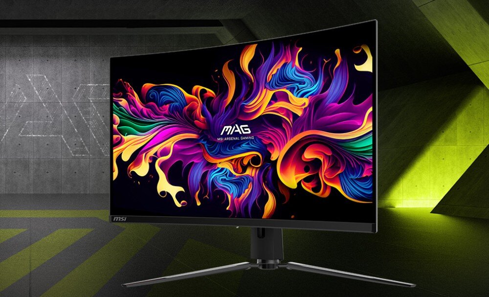 Monitor MSI Mag 321CUP QD-OLED Monitor z zakrzywionym ekranem widziany pod kątem na tle industrialnego wnętrza wyświetlający abstrakcyjną tapetę w żywych kolorach fioletu i pomarańczu, opis