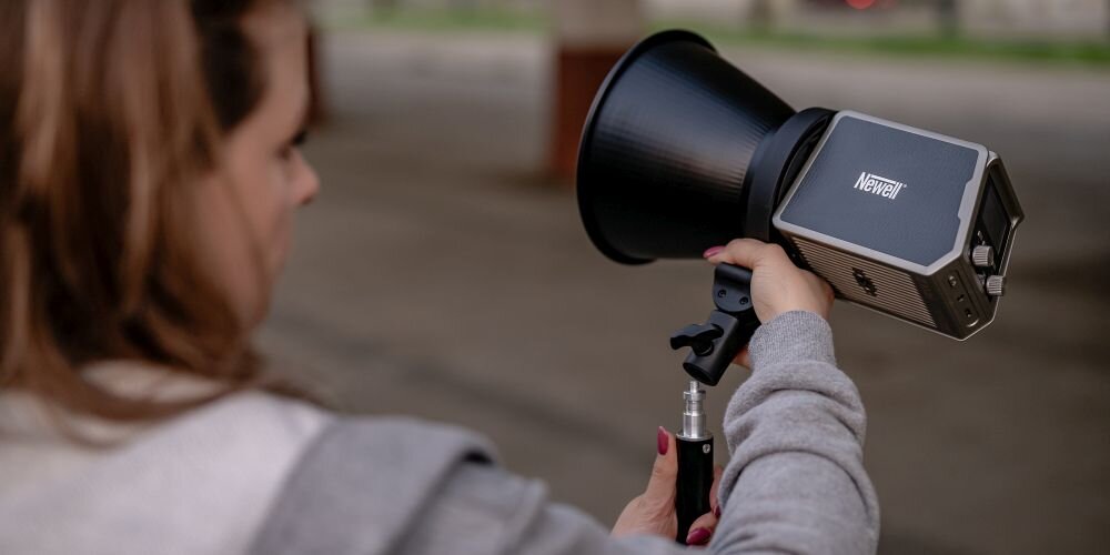 Kobieta montuje srebrną lampę Newell z czarną czaszą na statywie oświetleniowym w industrialnym wnętrzu.