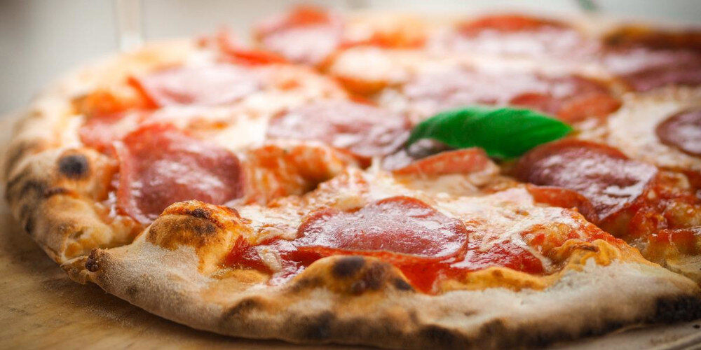 Na obrazie widoczna jest pizza z plasterkami pepperoni i liściem bazylii na wierzchu. Ciasto jest lekko przypieczone na brzegach.