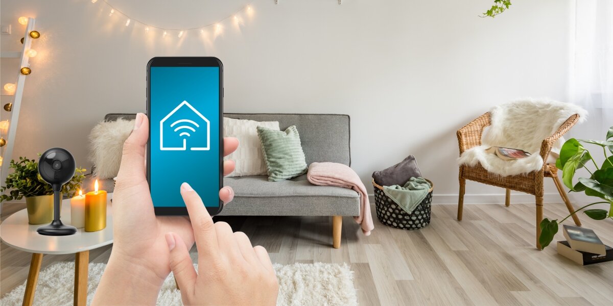 Kamera inteligentna HAMA 176651 Wewnętrzna, WLAN Czarny, aplikacje, polecenie, wyświetlacz, kamera, w tle pokój gościnny, osoba obsługuje smartfon z aplikacją