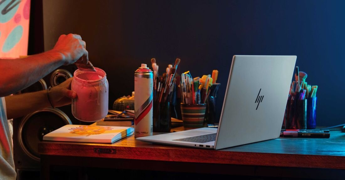 Mężczyzna korzysta z pędzla przy laptopie HP Envy x360, tworząc nietypową kompozycję artystyczną. Intel Core Ultra Turbo Boost