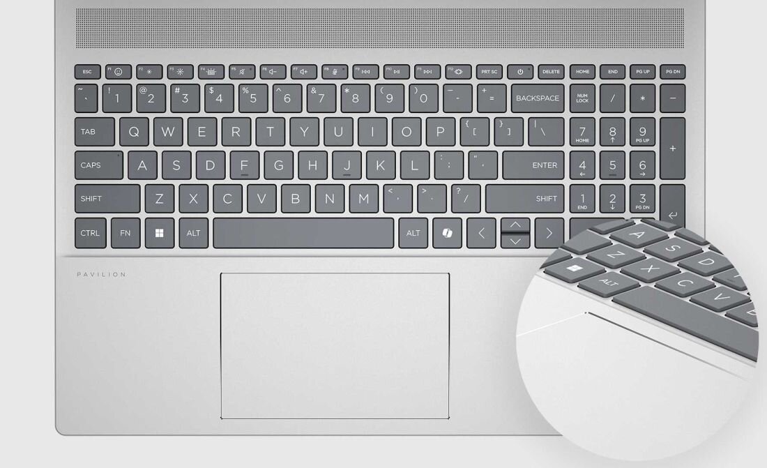Widok z góry na laptop HP Pavilion 16 w srebrnej obudowie z pełnowymiarową klawiaturą i dużym touchpadem, logo PAVILION widoczne pod ekranem, na jasnym tle z kółkiem powiększającym fragment klawiatury. - Pełnowymiarowa klawiatura z podświetleniem