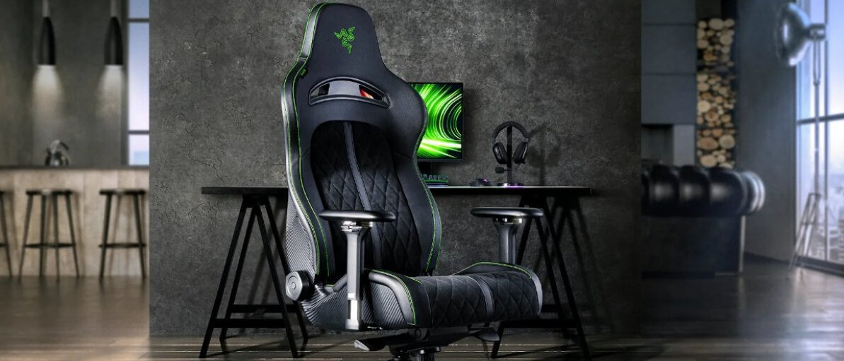 Czarno-zielony fotel gamingowy z logo Razer na oparciu stoi w nowoczesnym wnętrzu. W tle znajduje się biurko z monitorem i słuchawkami.