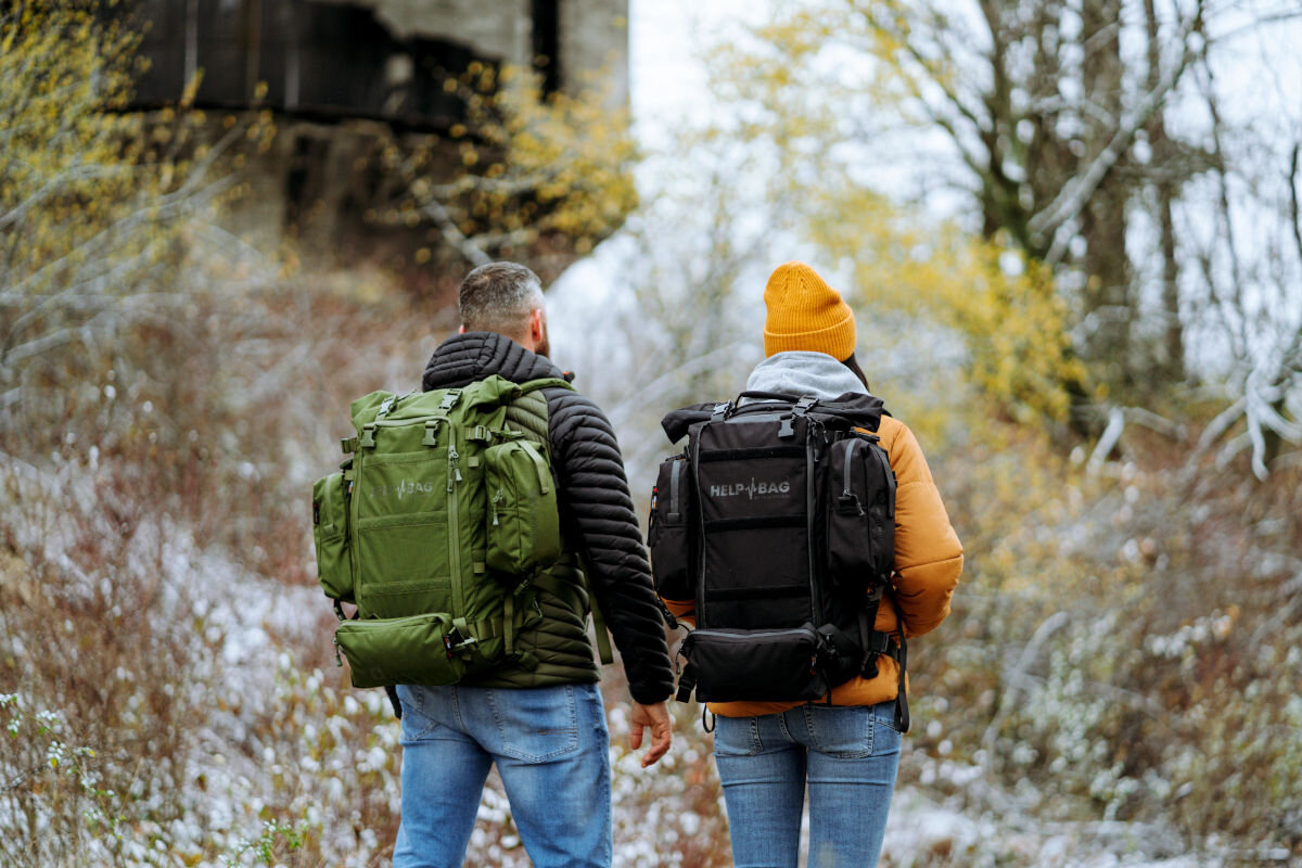 Plecak ewakuacyjny HELP BAG Max Zielony, zagrożenie, ewakuacja, survival, plecak, w tle las, para z plecakami na plecach spaceruje w zimowej aurze