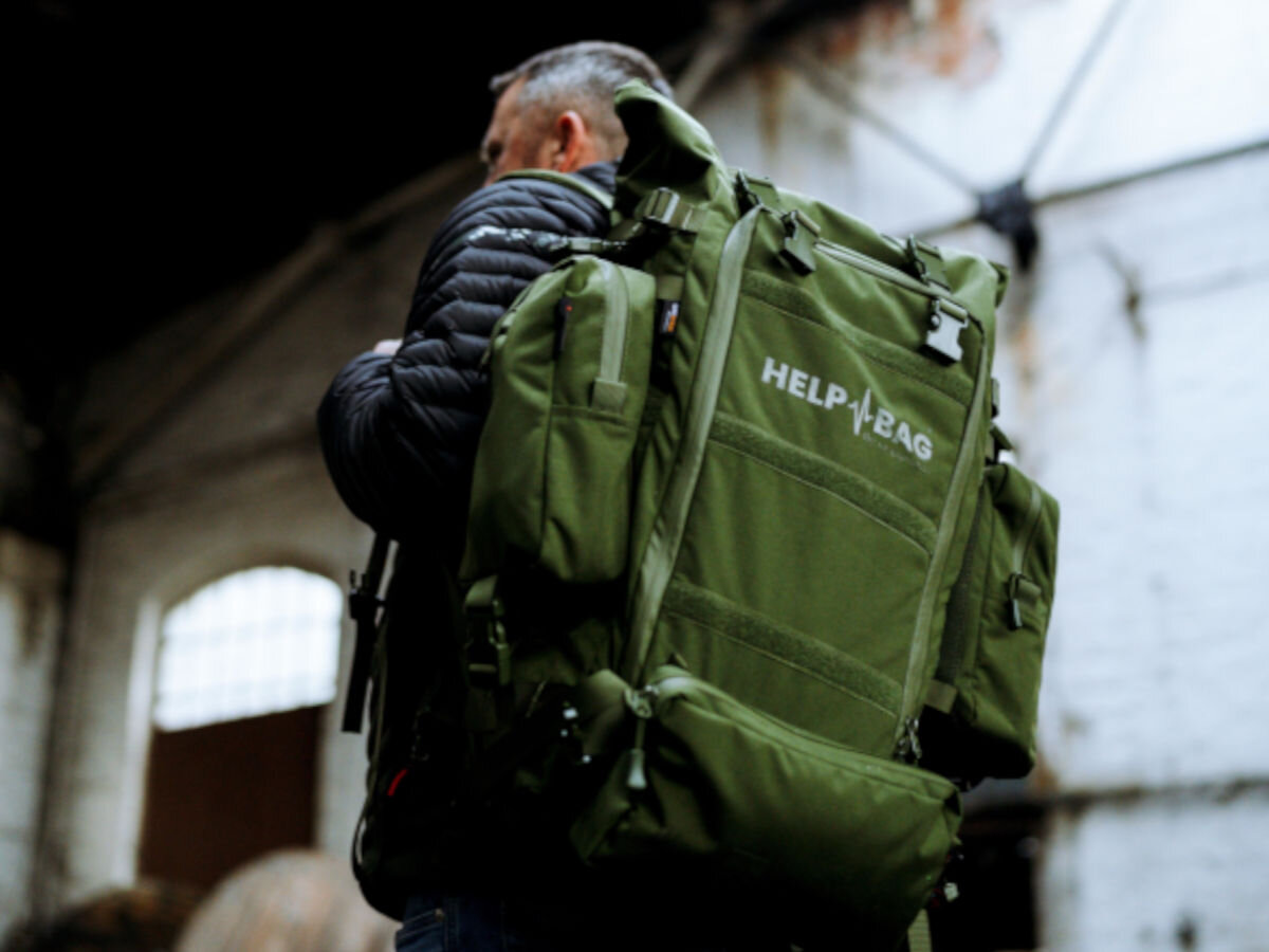 Plecak ewakuacyjny HELP BAG Max Zielony, moduły, akcesoria, rozmieszczenie, kolory, w tle środek opuszczonej fabryki, plecak helpbag zawieszony na ramieniu mężczyzny