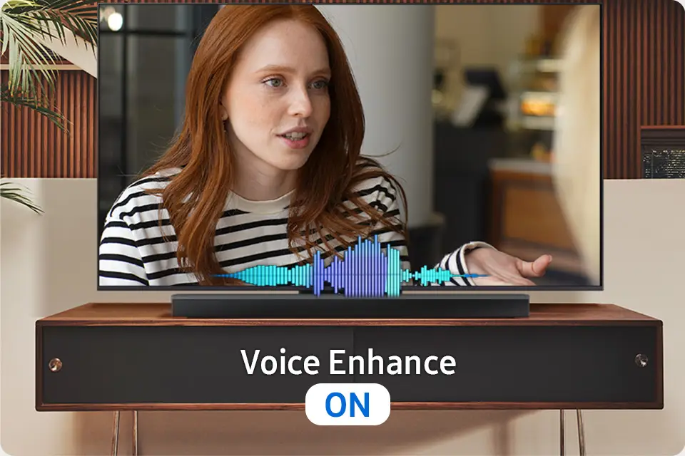 Na ekranie telewizora widać kobietę w biało-czarnej bluzce w paski, a przed nią znajduje się soundbar z wizualizacją dźwięku. Pod obrazem widnieje napis \'Voice Enhance ON\'.