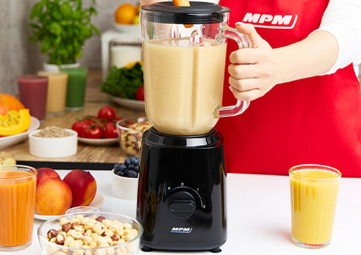 Kobieta miksuje koktajl w blenderze kielichowym MBL-37. Obok żywność i sok w szklankach.