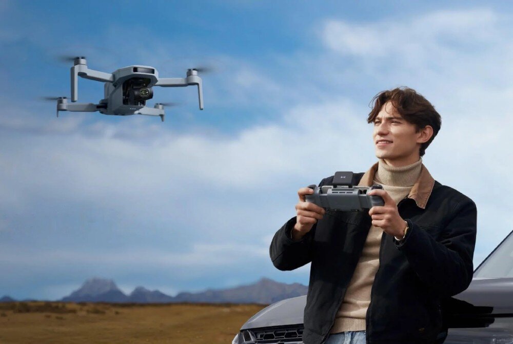 Dron POTENSIC Atom 2 Standard Kit Mężczyzna trzymający aparaturę sterującą obserwuje drona zawieszonego w powietrzu