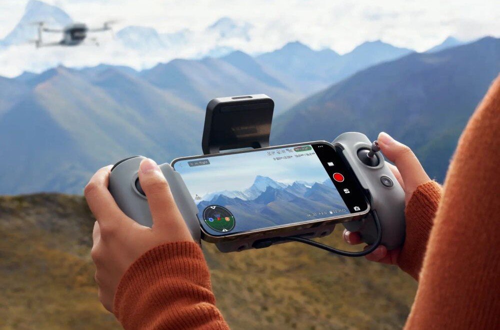 Dron POTENSIC Atom 2 Standard Kit Dłonie trzymające kontroler z telefonem pokazującym podgląd wideo na tle górskiego krajobrazu