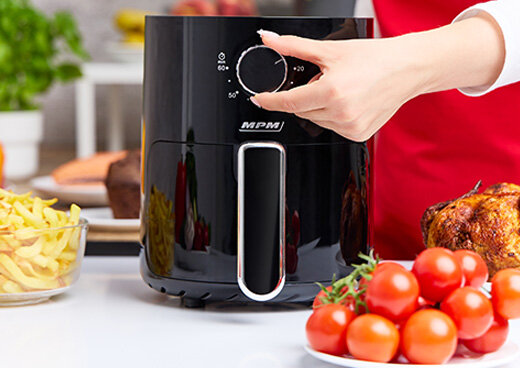 Frytkownica na kuchennym blacie. Osoba trzyma dłoń na pokrętle.