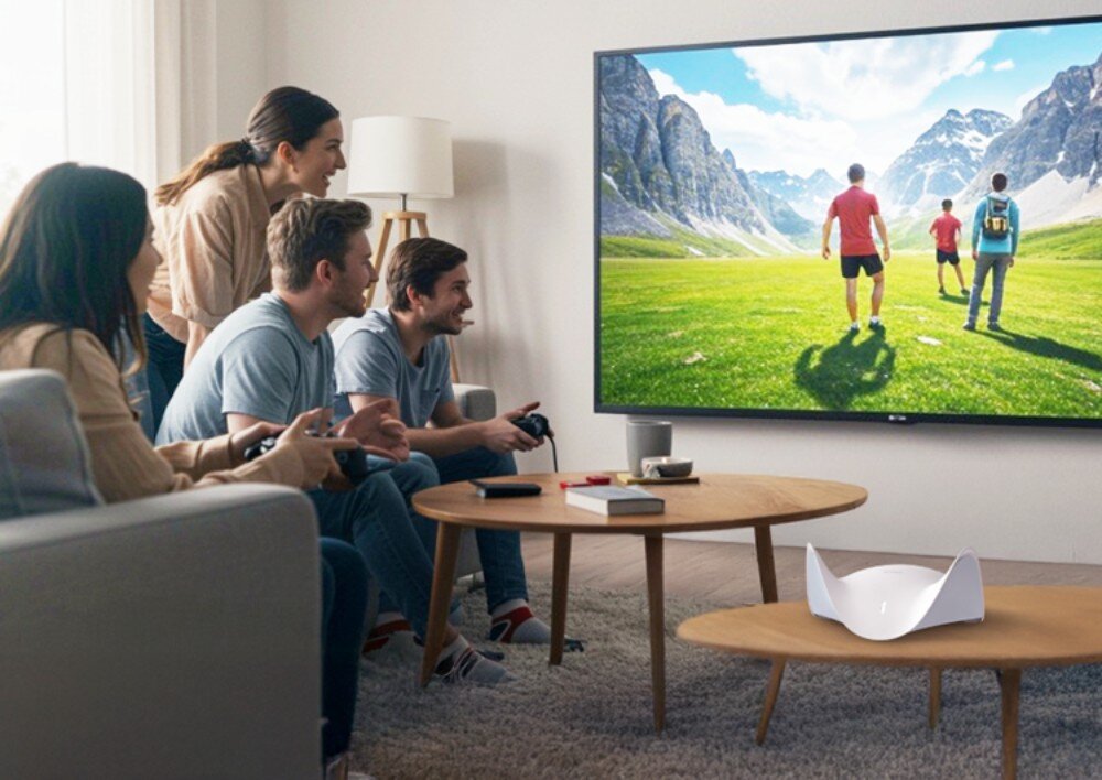 Router D-LINK BE9500 M95 Czworo młodych ludzi grających w gry i oglądających telewizję w salonie, w którym na pierwszym planie na stoliku kawowym umieszczono biały router