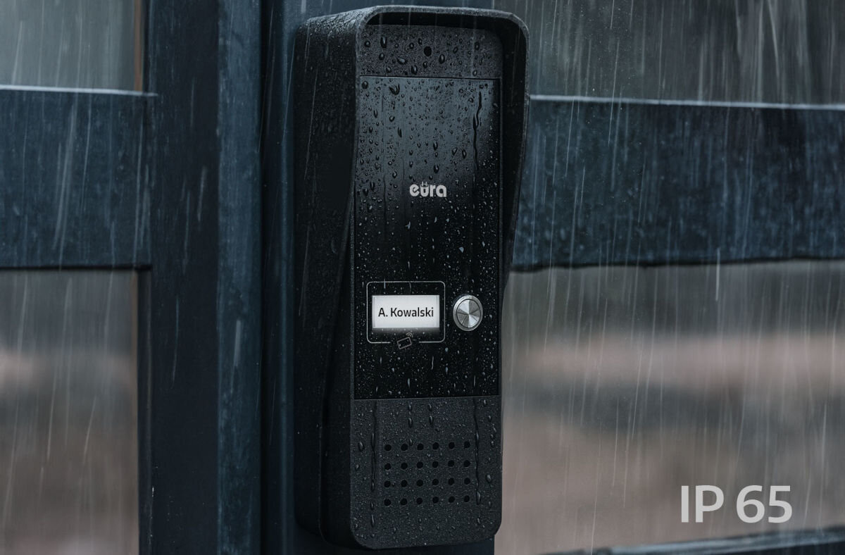 Domofon EURA ADP-25A3 Biały, szczelność, IP65, aluminium, odporność, Czarna kaseta bramowa domofonu Eura z daszkiem, w deszczu, z podświetlaną wizytówką „A. Kowalski”, przyciskiem dzwonka i oznaczeniem klasy szczelności IP65 w rogu.