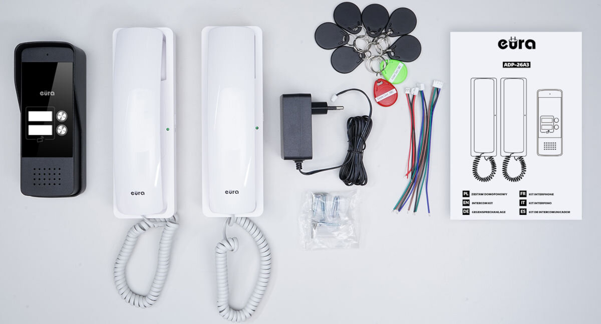 Domofon EURA ADP-26A3 Biały, zestaw, montaż, komplet, kompatybilność, Kompletny zestaw dwurodzinnego domofonu Eura – czarna kaseta bramowa z dwoma przyciskami, dwa białe unifony, zasilacz, breloki RFID, przewody, elementy montażowe i instrukcja obsługi ułożone na jasnym tle.