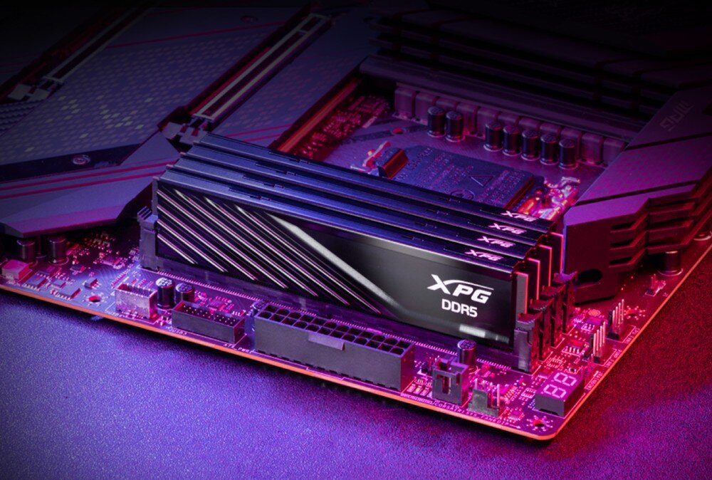 Pamięć RAM ADATA XPG Lancer Blade Cztery czarne moduły pamięci zamontowane w rzędzie na płycie głównej komputera, oświetlone fioletowym i czerwonawym światłem, widoczne są ukośne żłobienia na radiatorach, moduły, pojemność, taktowanie, opóźnienia