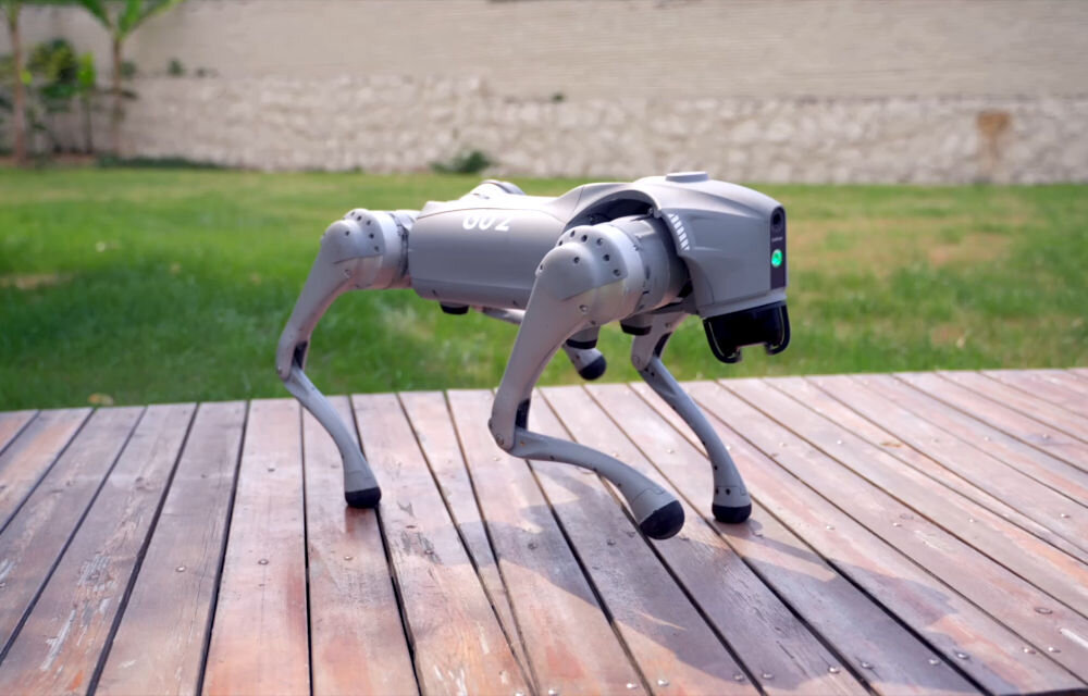 Robot pies UNITREE Go2 Air Czworonożny, szary robot Unitree GO2 stoi na drewnianej ścieżce na zewnątrz. Robot ma kształt psa i jest gotowy do poruszania się.