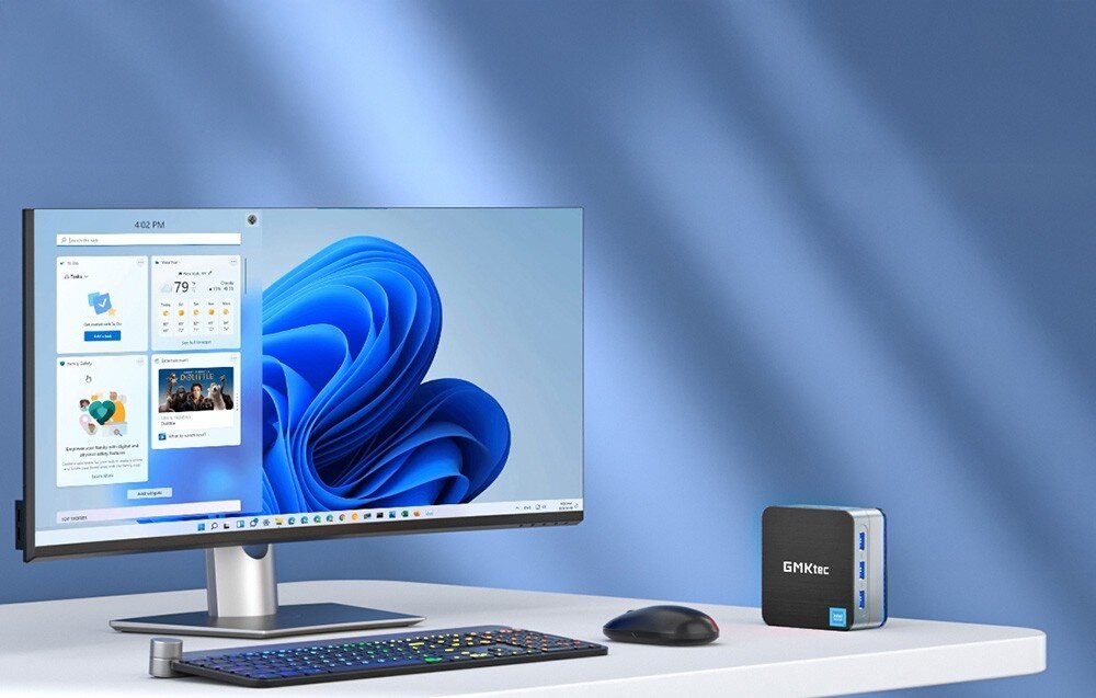Komputer GMKTEC G2 Plus Monitor z wyświetlonym pulpitem systemu obok niewielkiego komputera w formie kostki, klawiatury i myszki na biurku, opis