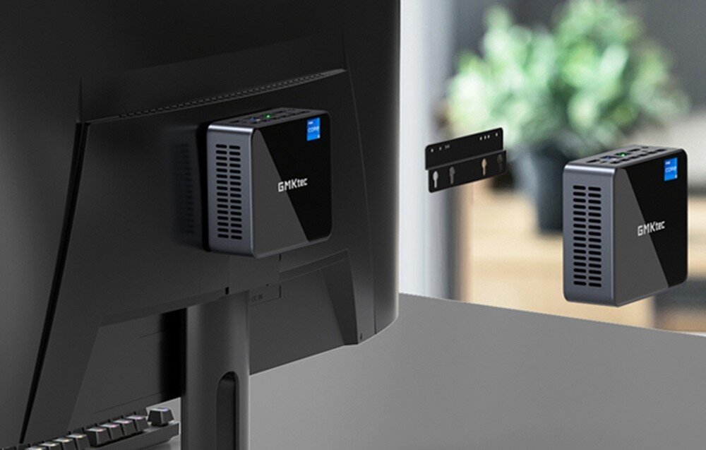 Komputer GMKTEC NucBox M3 Plus Mały komputer w czarnej obudowie zamontowany z tyłu monitora przy użyciu uchwytu ściennego, pamięć RAM, taktowanie