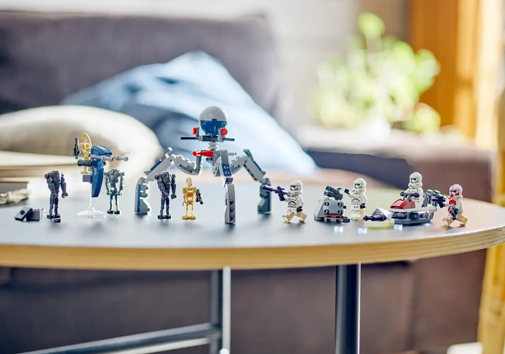 Na okrągłym stoliku znajdują się figurki LEGO przedstawiające postacie i pojazdy z serii Star Wars. W tle widoczna jest kanapa z poduszkami.