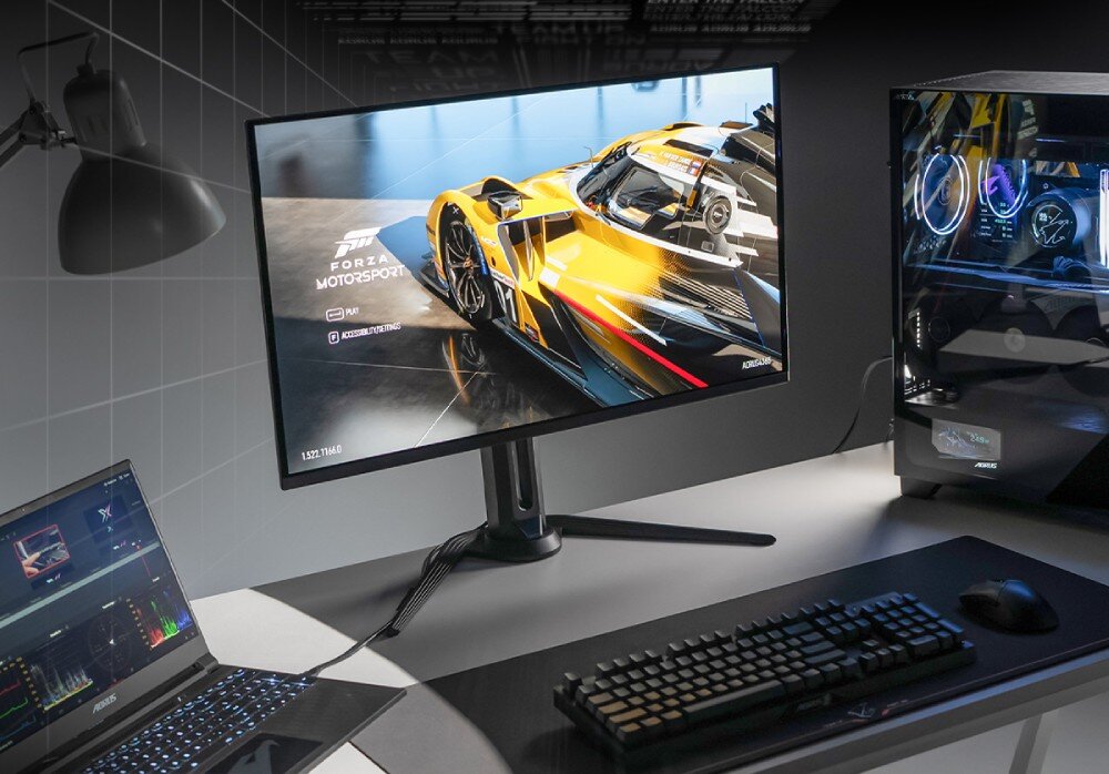 Monitor GIGABYTE Aorus FO27Q2 Monitor wyświetlający grę wyścigową na biurku obok laptopa i komputera stacjonarnego. Na ekranie menu gry Forza Motorsport, przełącznik KVM, obsługa